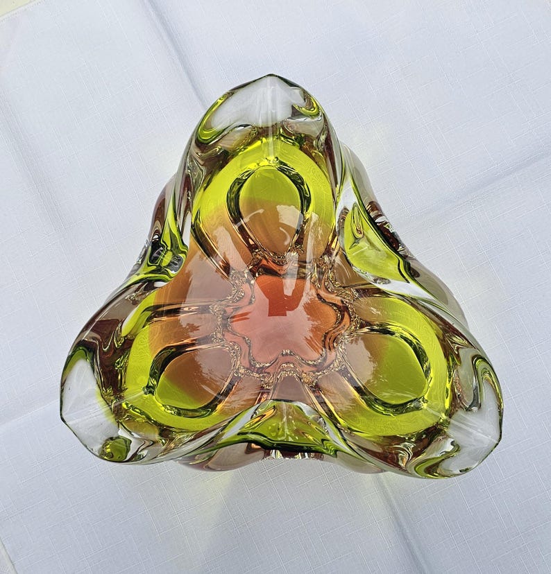May include: A triangular glass bowl featuring a vibrant lime green outer rim that transitions into a warm amber orange center. The thick, clear glass construction has a smooth, polished finish with three distinct rounded corners and a deep basin.