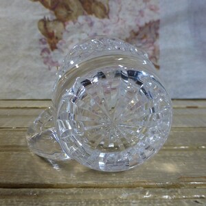 K&ouml;nnte beinhalten: Die Unterseite eines klaren Glaskrug mit einem geschliffenen Glasdesign. Der Krug hat einen runden Boden und einen Griff.