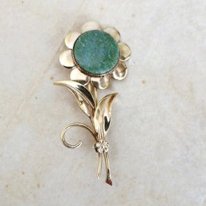 May include: A gold-tone brooch in the shape of a flower with a green stone center.