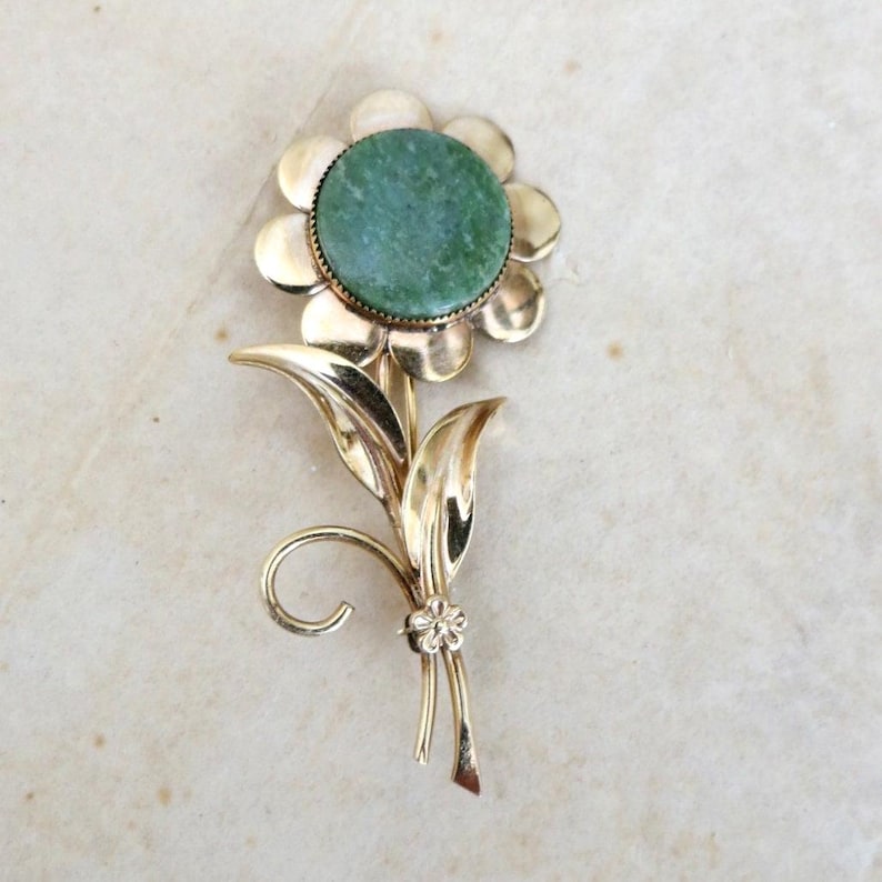 May include: A gold-tone brooch in the shape of a flower with a green stone center.
