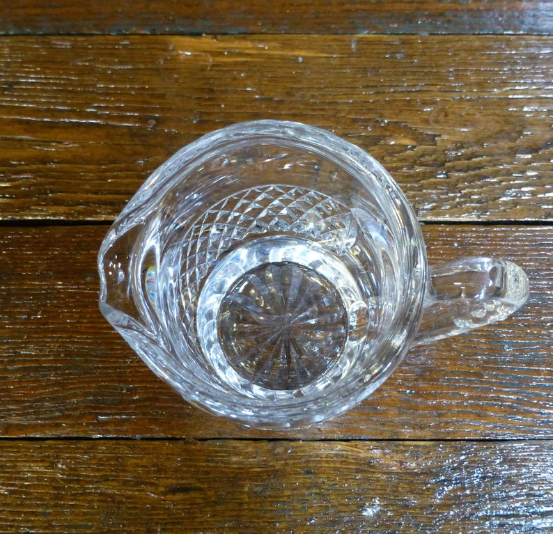 K&ouml;nnte beinhalten: Eine klare Glaskaraffe mit einem geschliffenen Glasdesign. Die Karaffe hat einen Henkel und eine breite &Ouml;ffnung.