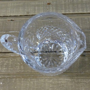 K&ouml;nnte beinhalten: Eine klare Glaskanne mit geschliffenem Glasdesign. Die Kanne hat einen Henkel und einen runden Boden.