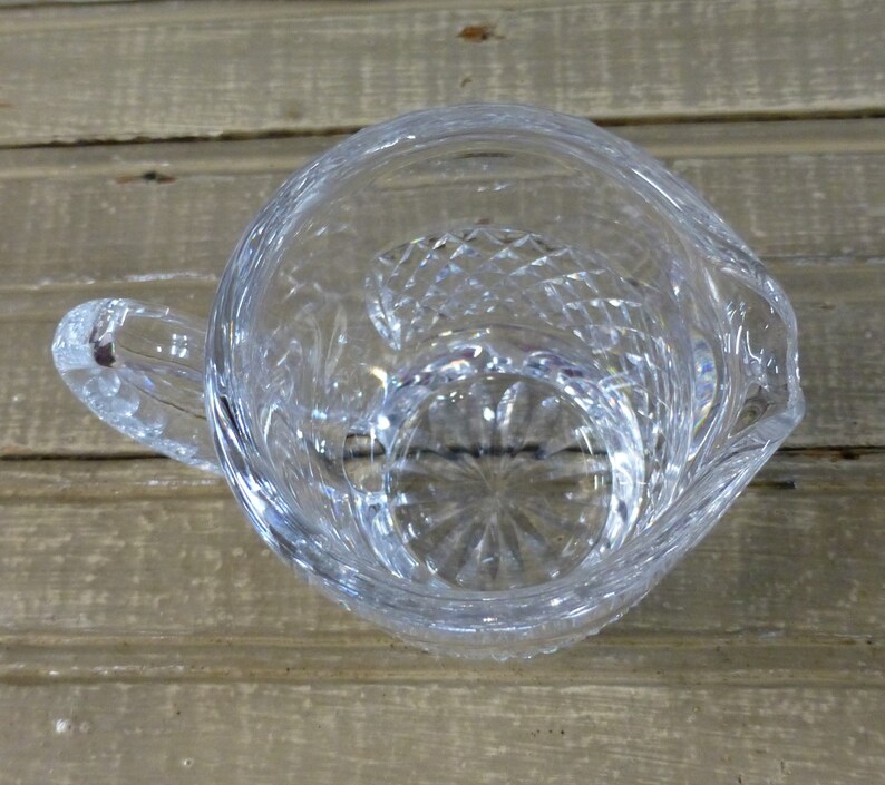 K&ouml;nnte beinhalten: Eine klare Glaskanne mit geschliffenem Glasdesign. Die Kanne hat einen Henkel und einen runden Boden.