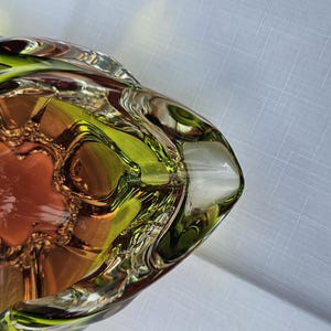 May include: A decorative glass bowl featuring a vibrant lime green outer rim that transitions into a warm amber orange center. The bowl has a distinct organic, undulating shape with thick, clear glass edges that create a layered, translucent effect.