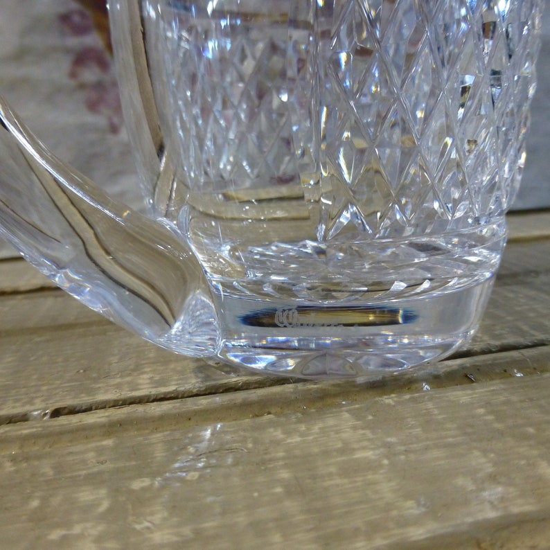 K&ouml;nnte beinhalten: Eine klare Glaskaraffe mit geschliffenem Glasdesign. Der Boden der Karaffe hat eine kleine ge&auml;tzte Markierung mit der Aufschrift "CCO."