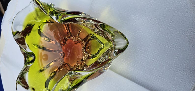 May include: A decorative glass bowl featuring a vibrant lime green outer rim that transitions into a warm amber and orange center. The bowl has a distinct triangular shape with undulating, ruffled edges and a smooth, polished finish throughout.