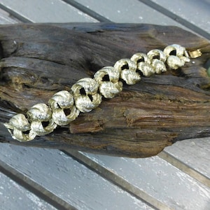May include: A gold-toned bracelet with a woven design. The bracelet is made of metal and has a clasp closure.