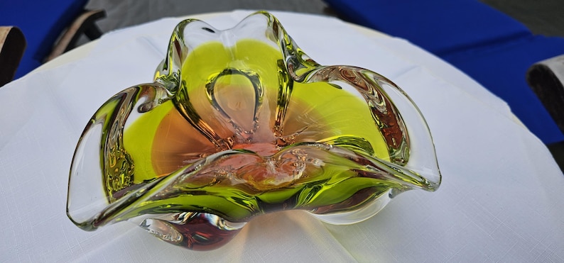 May include: A decorative glass bowl featuring a vibrant chartreuse green rim that transitions into a warm amber center. The bowl has a distinct organic, free-form shape with undulating, ruffled edges and a smooth, polished finish throughout.