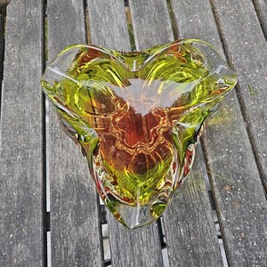 May include: A heart-shaped glass bowl featuring a vibrant gradient of lime green and amber tones. The thick, clear glass has a smooth, polished surface with organic, undulating edges that create a multi-faceted, reflective appearance throughout.