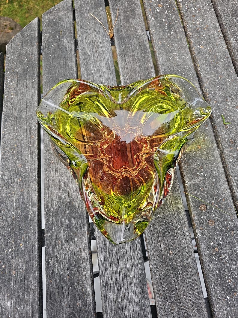 May include: A heart-shaped glass bowl featuring a vibrant gradient of lime green and amber tones. The thick, clear glass has a smooth, polished surface with organic, undulating edges that create a multi-faceted, reflective appearance throughout.