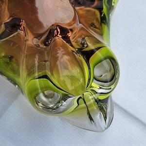 May include: A decorative glass bowl featuring a vibrant gradient of lime green and amber tones. The bowl has a thick, clear glass rim and a complex, multi-faceted organic shape with deep indentations and smooth, rounded protrusions throughout.