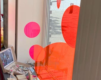 May include: A jewelry store display featuring various earrings, necklaces, and bracelets. The display includes open boxes and a wooden jewelry holder. Bright pink and orange circular decorations hang in the window.