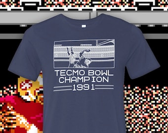 May include: A navy blue t-shirt with a white graphic of a video game scene. The text "Tecmo Bowl Champion 1991" is printed on the shirt.