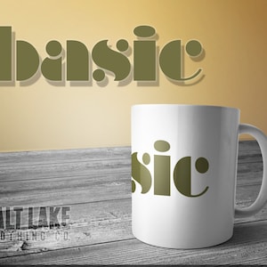 Könnte beinhalten: Eine weiße Keramiktasse mit einer grünen Grafik des Wortes "basic" darauf. Die Tasse steht auf einer Holzoberfläche. Die Worte "SALT LAKE CLOTHING CO." sind in der linken unteren Ecke des Bildes zu sehen.