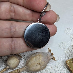 May include: A silver oval pendant with a smooth, shiny surface. The pendant is attached to a silver chain with a clasp.
