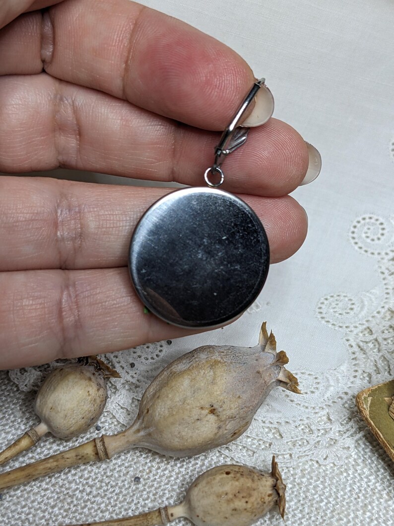 May include: A silver oval pendant with a smooth, shiny surface. The pendant is attached to a silver chain with a clasp.