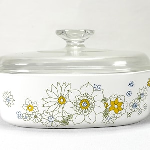 May include: White oval casserole dish with a clear glass lid. The dish is decorated with a floral pattern in yellow, blue, and green. The lid has a clear glass handle.