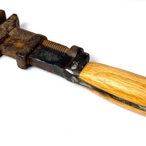 May include: An antique adjustable wrench with a wooden handle. The metal components are heavily rusted, showing signs of age and use. The handle is a light-colored wood, contrasting with the dark metal. The wrench is designed for tightening or loosening bolts and nuts.