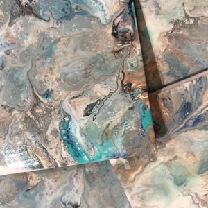 May include: Abstract art coasters with a swirling pattern of blue, gray, and white paint. The coasters have a glossy finish and are perfect for adding a touch of modern style to any home.