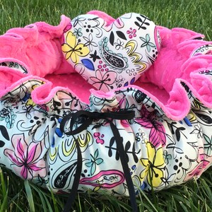 May include: A pink and white pet bed with a heart-shaped pillow. The bed is made of soft fabric with a floral pattern and has a black ribbon tie.