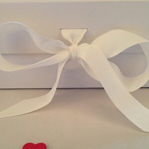 May include: A white gift box with a white satin ribbon tied in a bow.