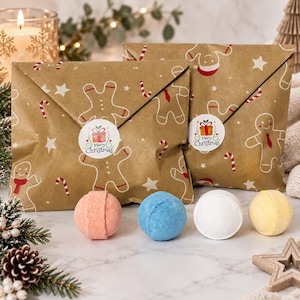 Puede incluir: Dos sobres de papel marrón con un patrón de hombres de jengibre, bastones de caramelo y estrellas, sellados con una pegatina redonda de Merry Christmas. Cuatro bombas de baño esféricas en color melocotón, azul, blanco y amarillo.