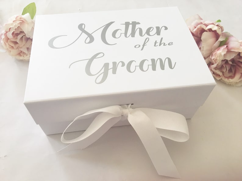 May include: White gift box with a white satin ribbon tied in a bow. The box has the words "Mother of the Groom" printed in silver on the top.