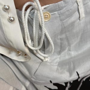 Puede incluir: Primer plano de una camisa y pantal&oacute;n azul claro con botones de perlas blancas y un cord&oacute;n blanco. El pantal&oacute;n tiene cierre de bot&oacute;n y un bolsillo. La camisa tiene cuello y pu&ntilde;os blancos.