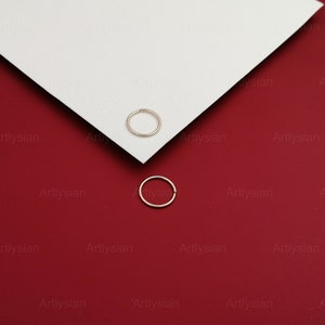 May include: Two silver nose rings on a red and white background.