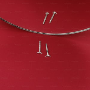 May include: Two pairs of silver stud earrings with a triangular shape at the bottom. The earrings are displayed on a red surface.