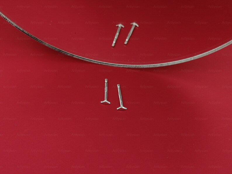 May include: Two pairs of silver stud earrings with a triangular shape at the bottom. The earrings are displayed on a red surface.