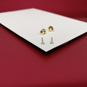May include: Two pairs of gold triangle stud earrings on a white surface.