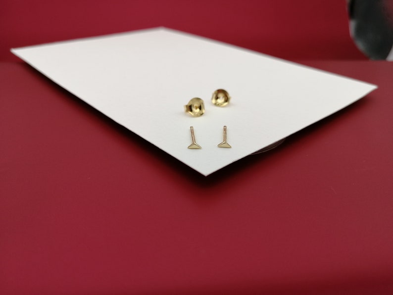 May include: Two pairs of gold triangle stud earrings on a white surface.