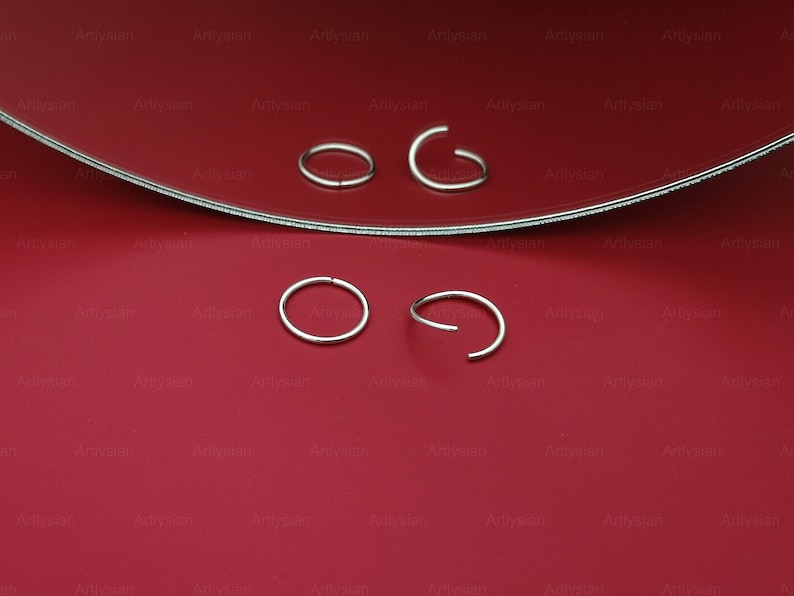 May include: Four silver nose rings on a red surface. Two of the nose rings are closed circles and two are open circles.