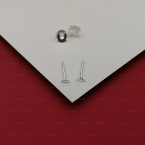 May include: Two silver triangle stud earrings on a white surface. The earrings are small and simple, with a triangular shape and a post that goes through the earlobe.