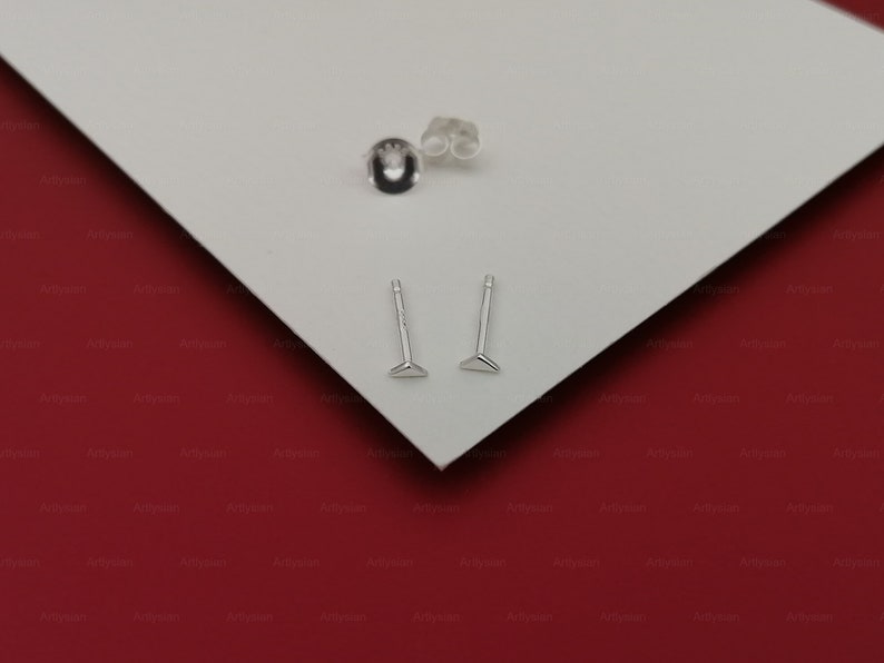 May include: Two silver triangle stud earrings on a white surface. The earrings are small and simple, with a triangular shape and a post that goes through the earlobe.