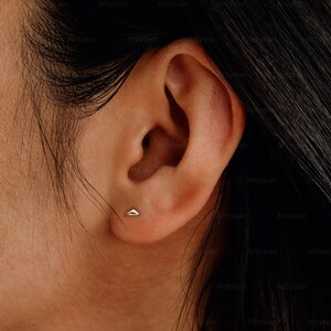 May include: A gold triangle stud earring in a person's earlobe.