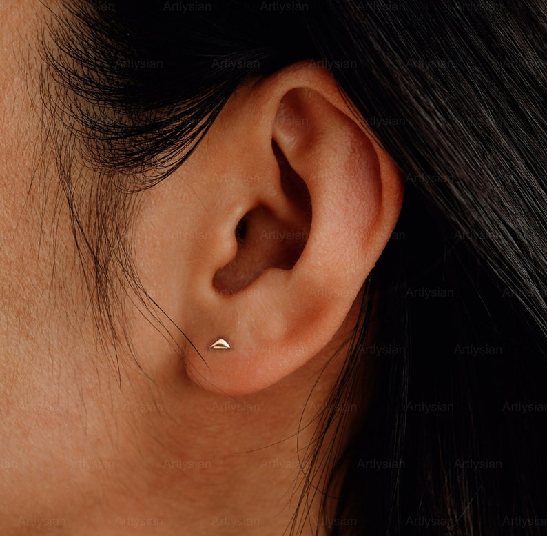 May include: A gold triangle stud earring in a person's earlobe.