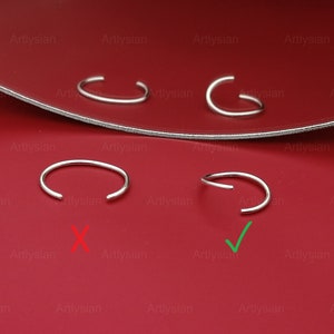 May include: Four silver nose rings on a red surface. Two of the nose rings are marked with a green checkmark, and two are marked with a red X. The nose rings are open hoop style.