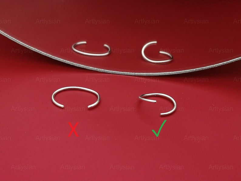 May include: Four silver nose rings on a red surface. Two of the nose rings are marked with a green checkmark, and two are marked with a red X. The nose rings are open hoop style.