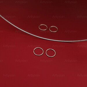 May include: Four silver hoop earrings on a red surface. The hoops are arranged in two pairs, with each pair slightly offset from the other.