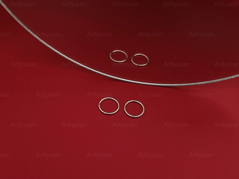 May include: Four silver hoop earrings on a red surface. The hoops are arranged in two pairs, with each pair slightly offset from the other.