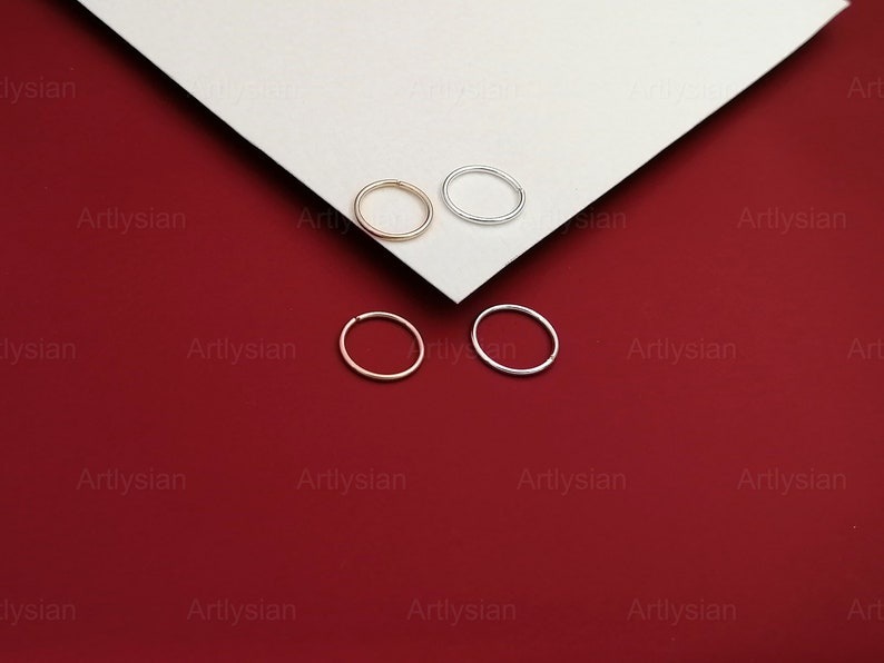 May include: Four hoop earrings, two silver and two gold, displayed on a white surface against a red background.