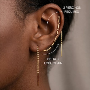 May include: A gold-toned chain earring connecting a lobe piercing to a helix piercing, featuring small cylindrical beads along the chain and straight bar ends. Text on the image reads 2 PIERCINGS REQUIRED and HELIX LOBE CHAIN.