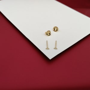 May include: Two pairs of gold stud earrings. One pair is a small round stud and the other pair is a small triangle stud.