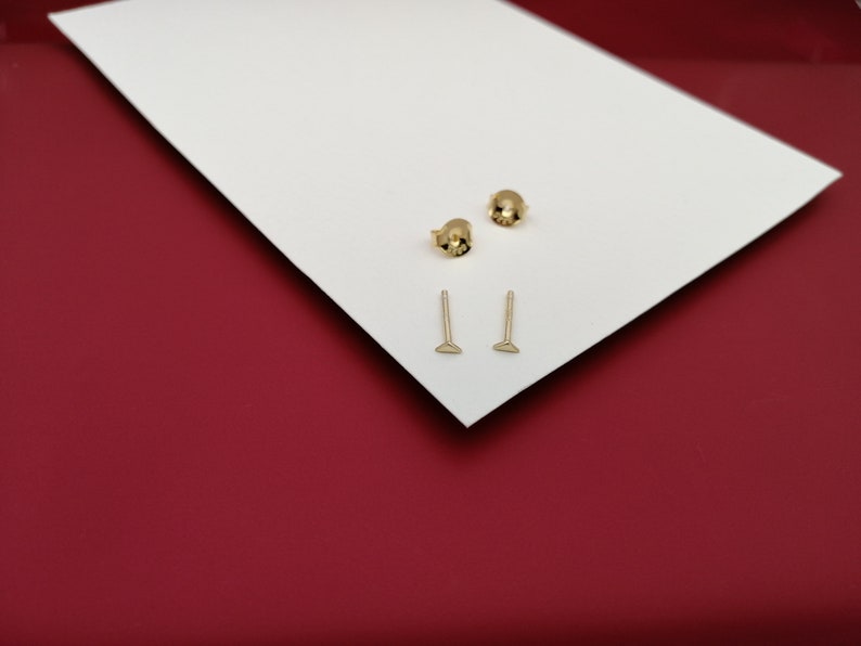May include: Two pairs of gold stud earrings. One pair is a small round stud and the other pair is a small triangle stud.