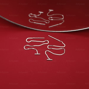 Op de afbeelding: Zilveren oorhangers met een T-bar design en een delicate ketting. De oorbellen worden gepresenteerd op een rode ondergrond met een zilveren rand. Een eenvoudig en elegant accessoire.