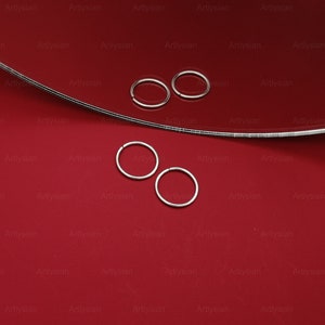 May include: Four silver hoop earrings on a red surface. The hoops are all the same size and have a simple, circular design.
