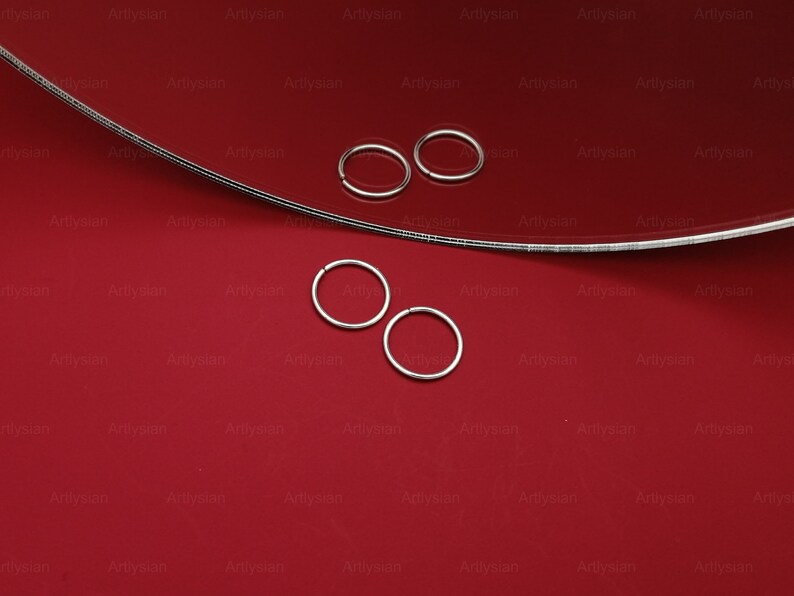 May include: Four silver hoop earrings on a red surface. The hoops are all the same size and have a simple, circular design.
