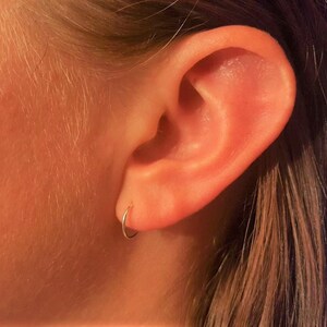 May include: A close-up of a person's ear with a small silver hoop earring in the lobe.